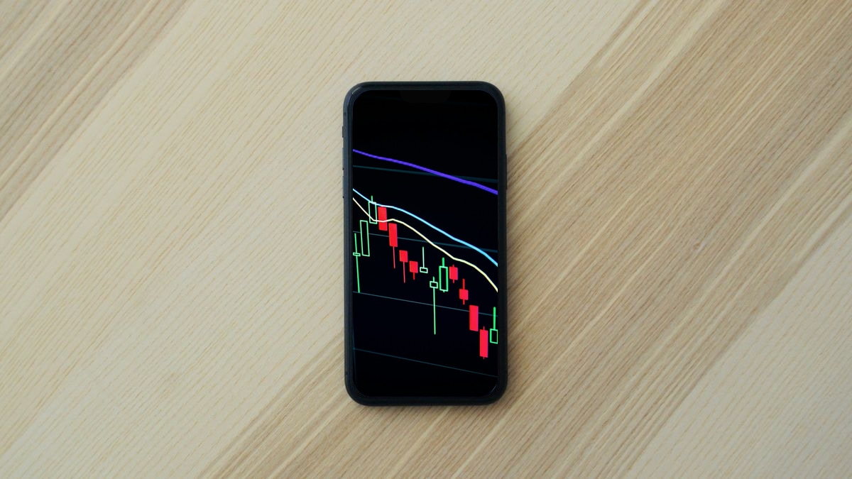 Ahşap çalışma masasında akıllı telefon ekranında yükselen finansal gelir grafikleri ve mobil uygulama analitiği